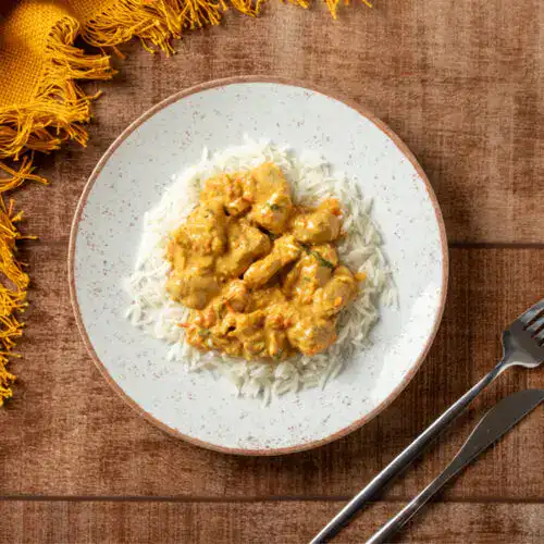 Prato de frango ao curry com arroz basmati em prato branco.