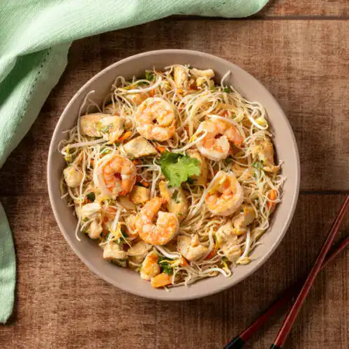 Prato de Pad Thai com camarão, frango e noodles em tigela.